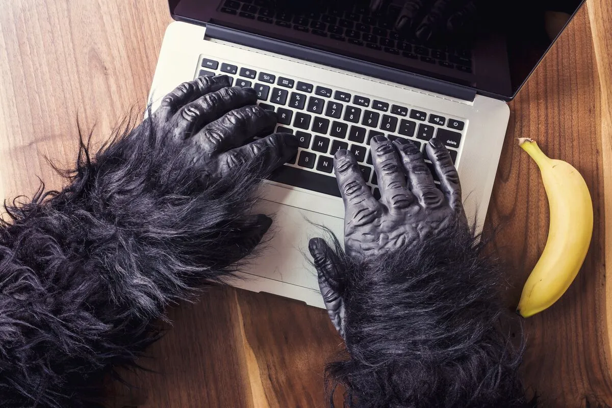 Gorilla-costume hands typing on a laptop keyboard, a banana on the desk beside them.
